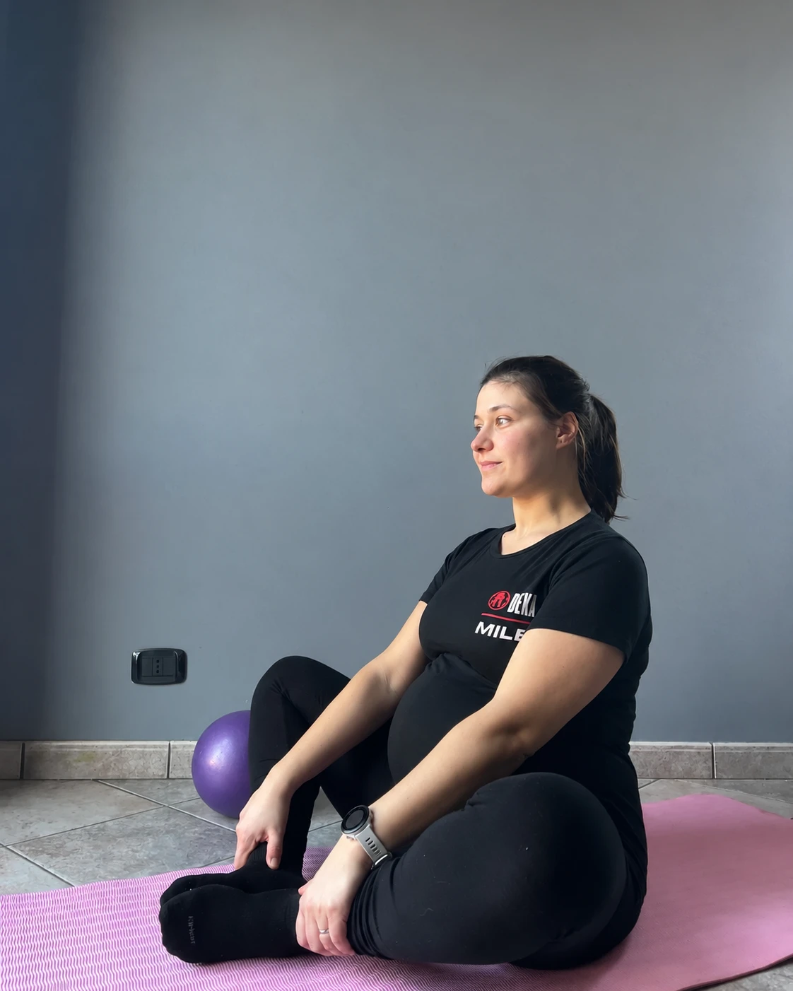 Cliente in gravidanza seduta sul tappetino con una piccola palla, in allenamento